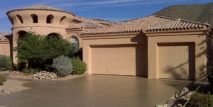 The exterior of a home with stucco siding has a concrete driveway coating with epoxy leading up to a three-car garage.