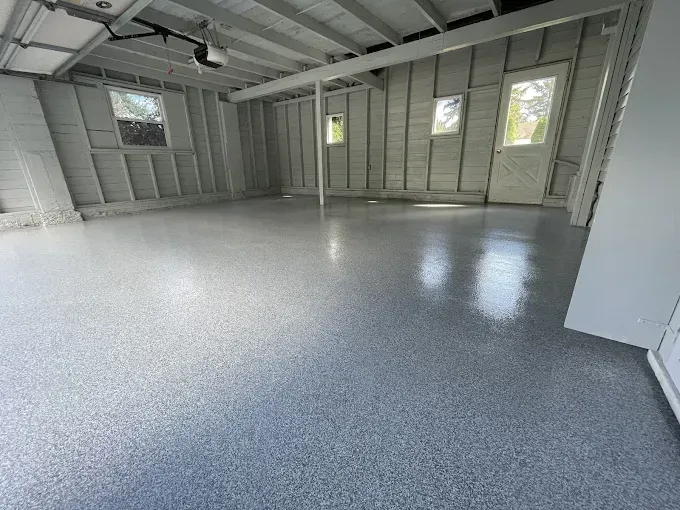 Garage with gray full flake epoxy floor, exposed wood ceiling beams, and a white door