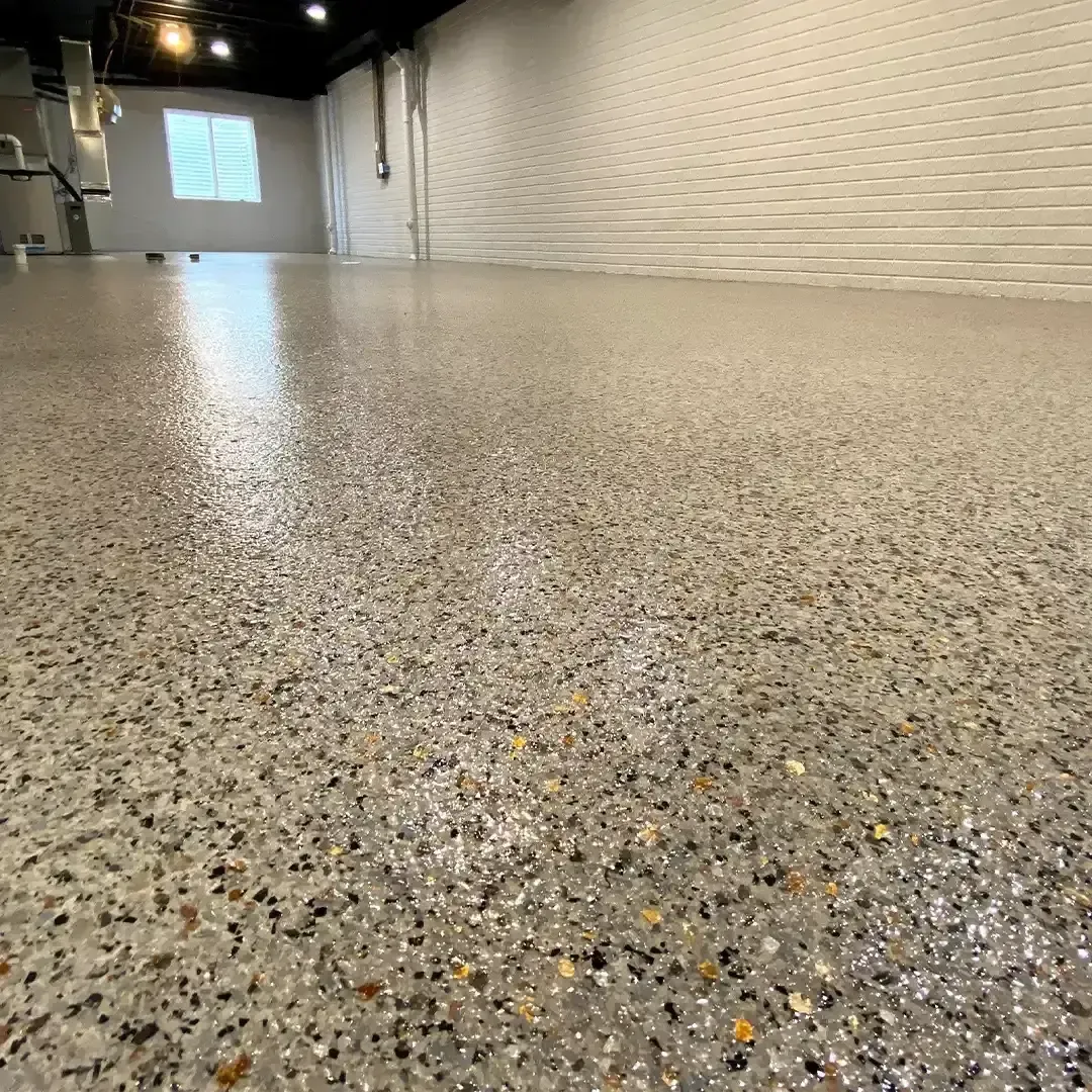 Technician applying epoxy floor coating to a garage floor with an open overhead door