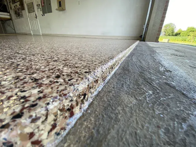 Garage threshold showing a full flake epoxy floor beside bare gray concrete driveway