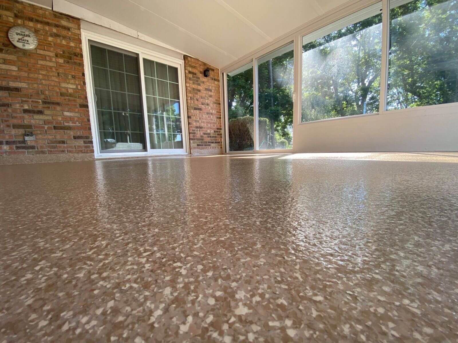 Full flake epoxy floor coating on an enclosed porch with a brick wall and sliding glass door