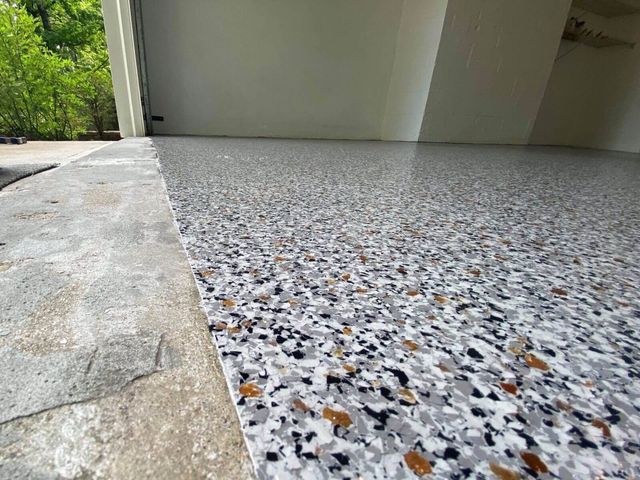 Full flake epoxy garage floor beside an open garage door with driveway and trees outside