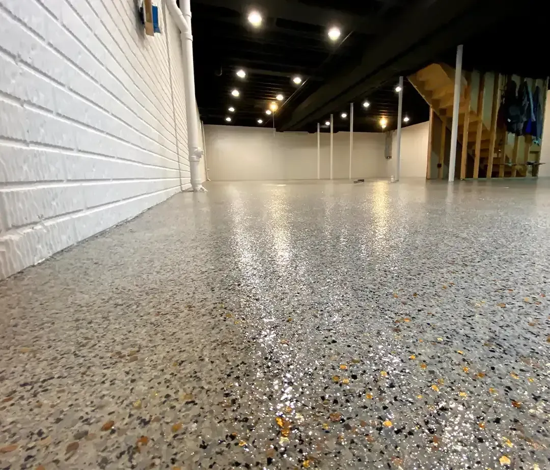 Full flake epoxy floor coating in an open basement with white brick walls and a staircase