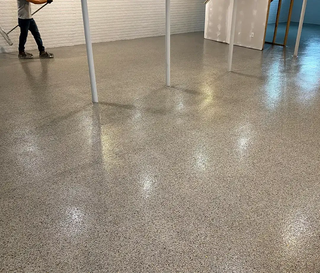 Gray full flake epoxy basement floor around steel support columns with an installer in spiked shoes