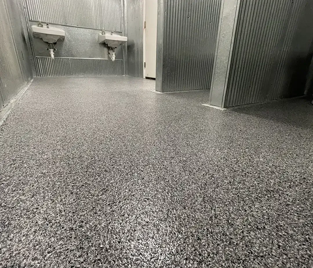 Full flake epoxy floor in an industrial washroom with corrugated metal walls and two sinks