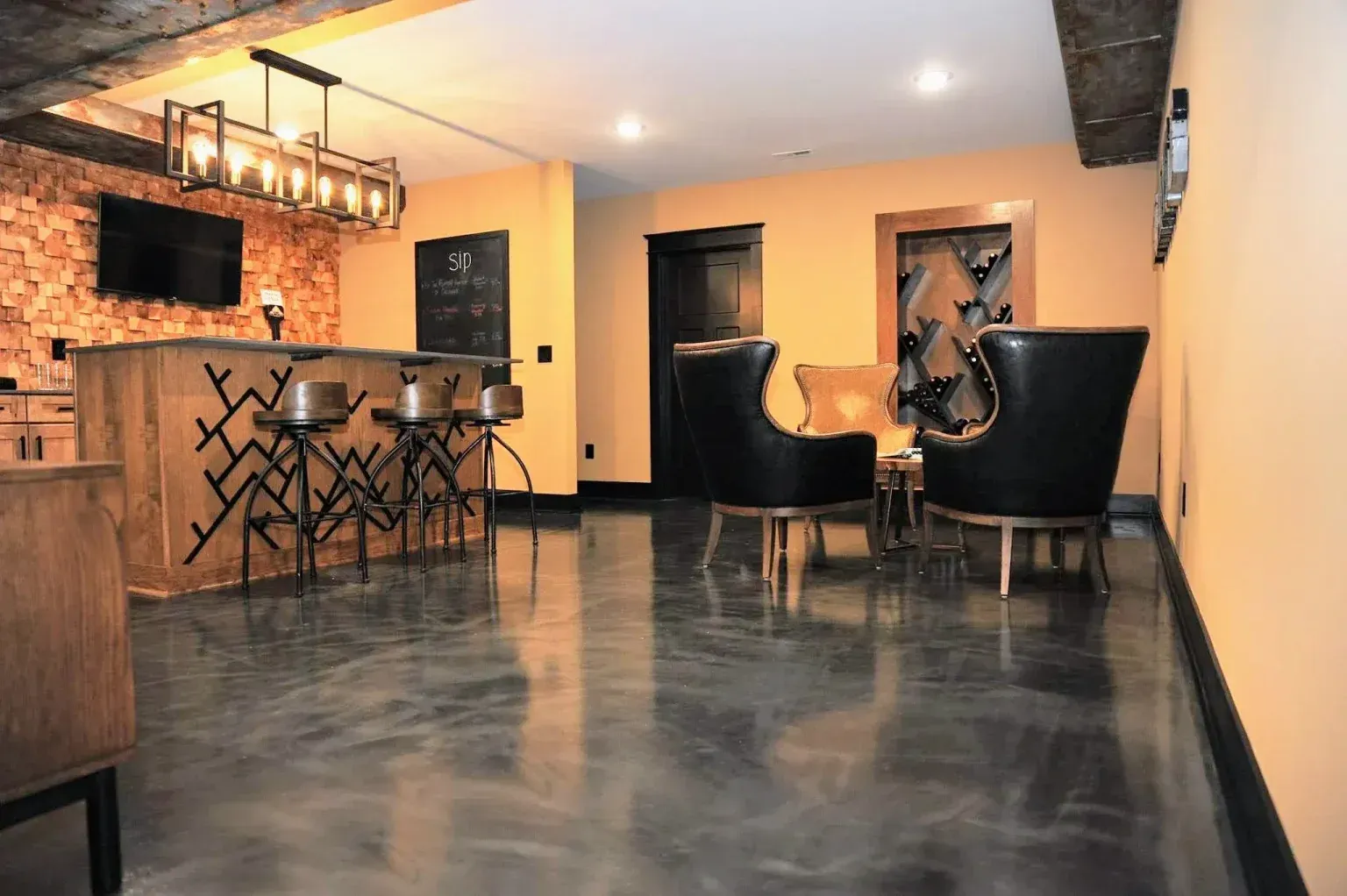 Basement bar and lounge with black leather chairs and a metallic epoxy floor