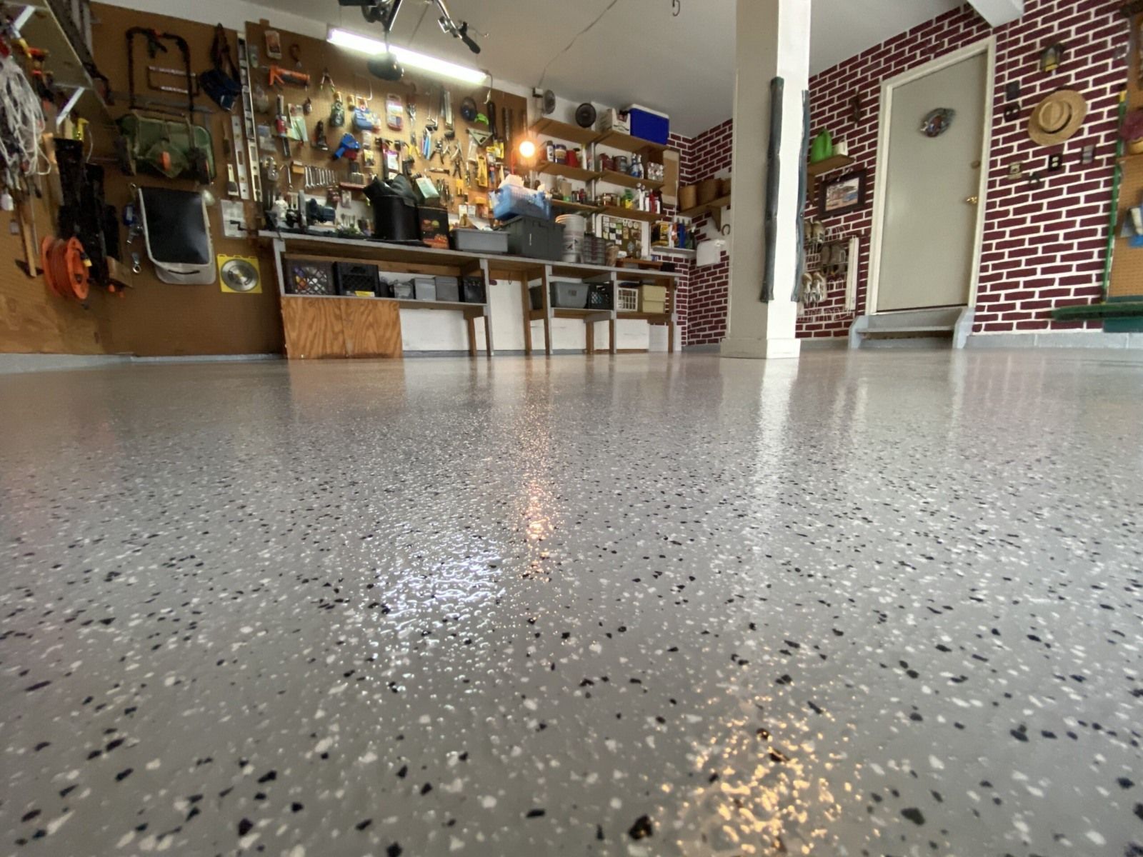 Workshop garage with a pegboard tool wall, brick accent wall, and full flake epoxy floor