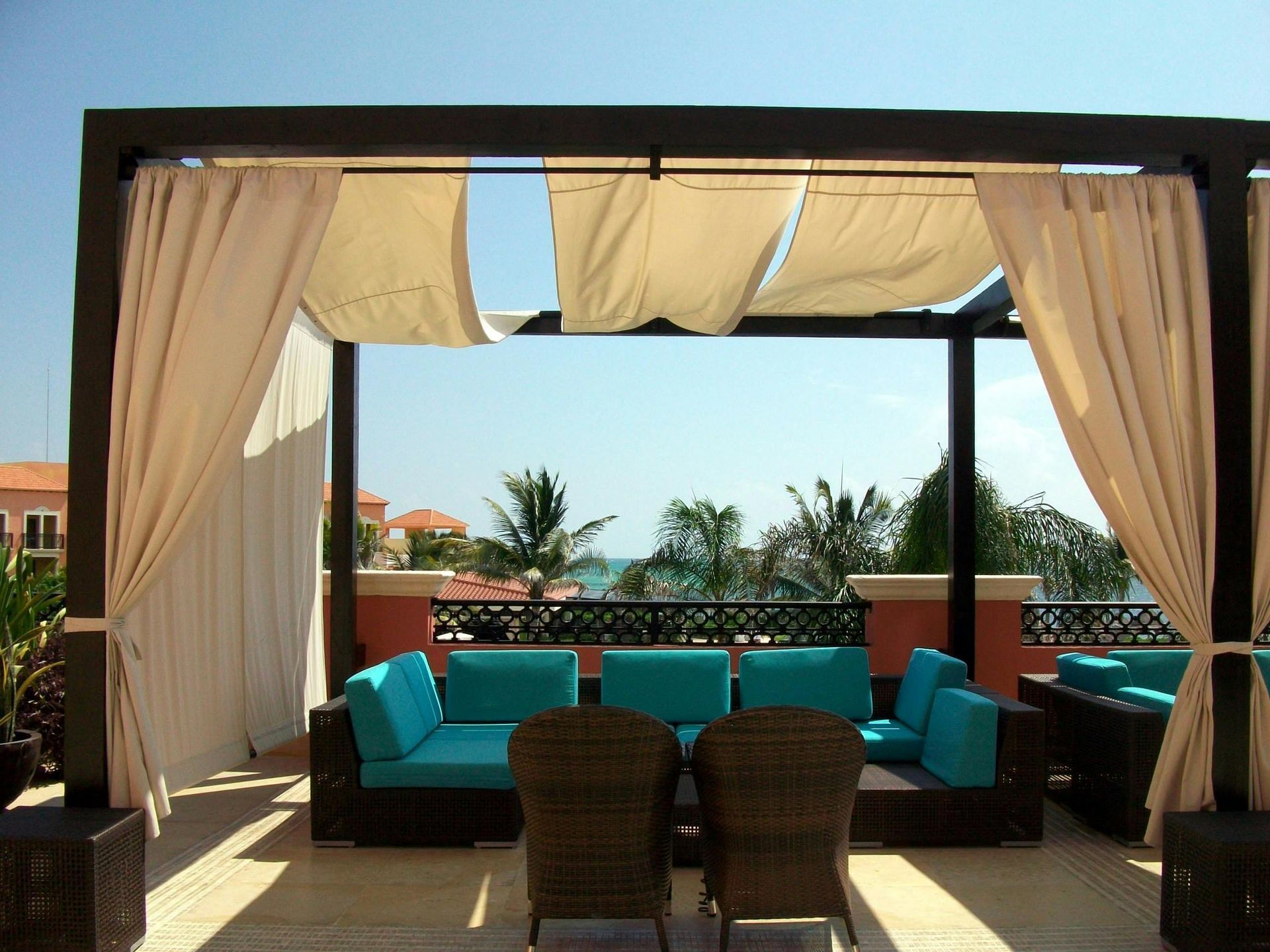 Outdoor cabana lounge with turquoise cushions overlooking palm trees and the ocean