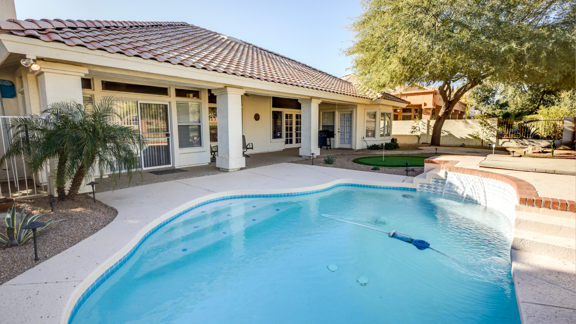 Backyard swimming pool with a stucco house, tile roof, and palm tree