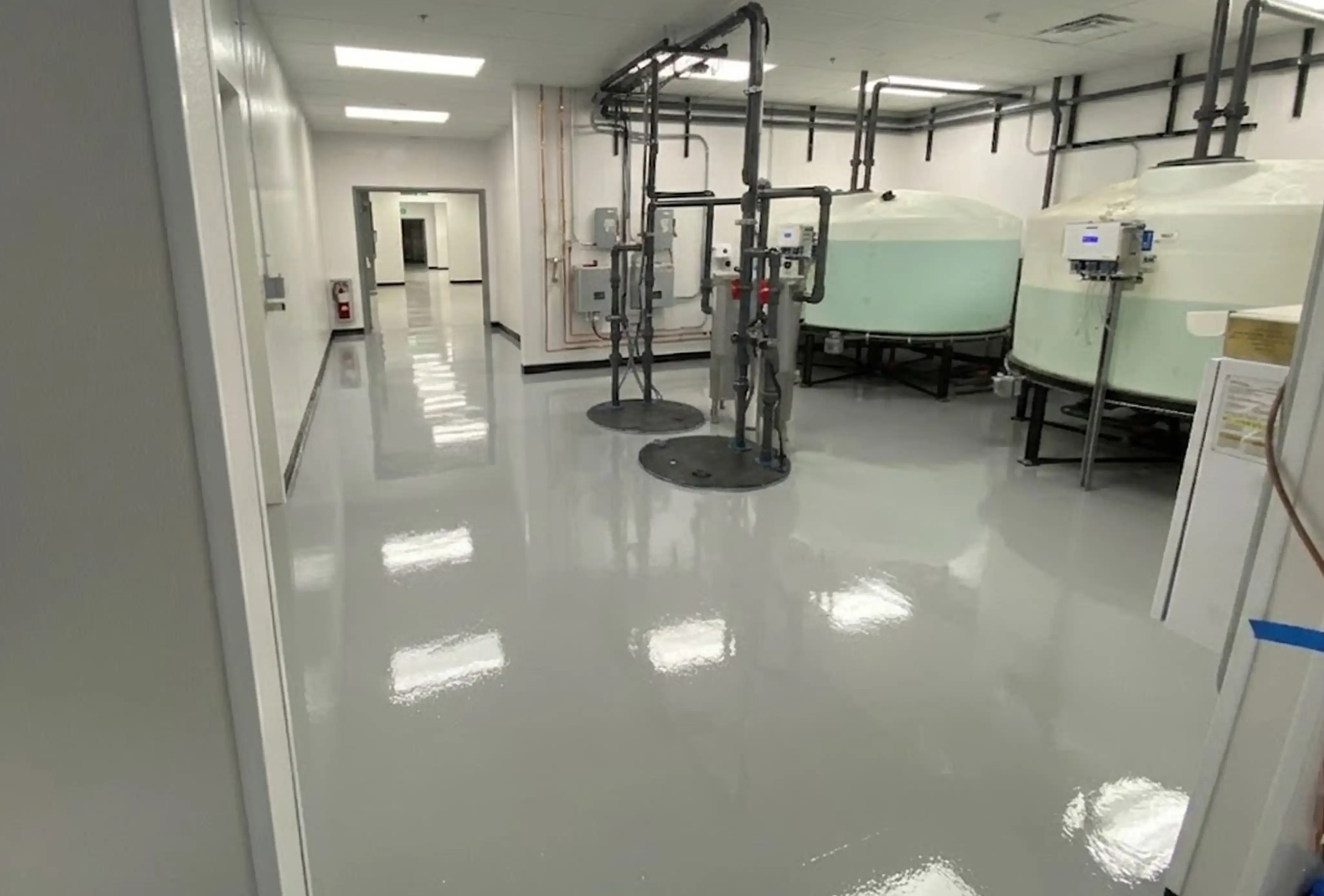 Commercial hallway with mixing tanks and piping on a glossy gray epoxy floor coating