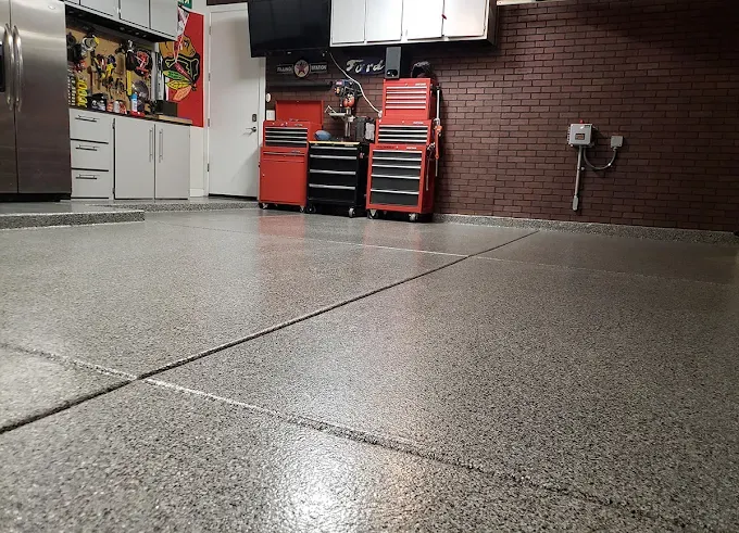 Garage with red rolling tool chests, a brick accent wall, and a gray full flake epoxy floor