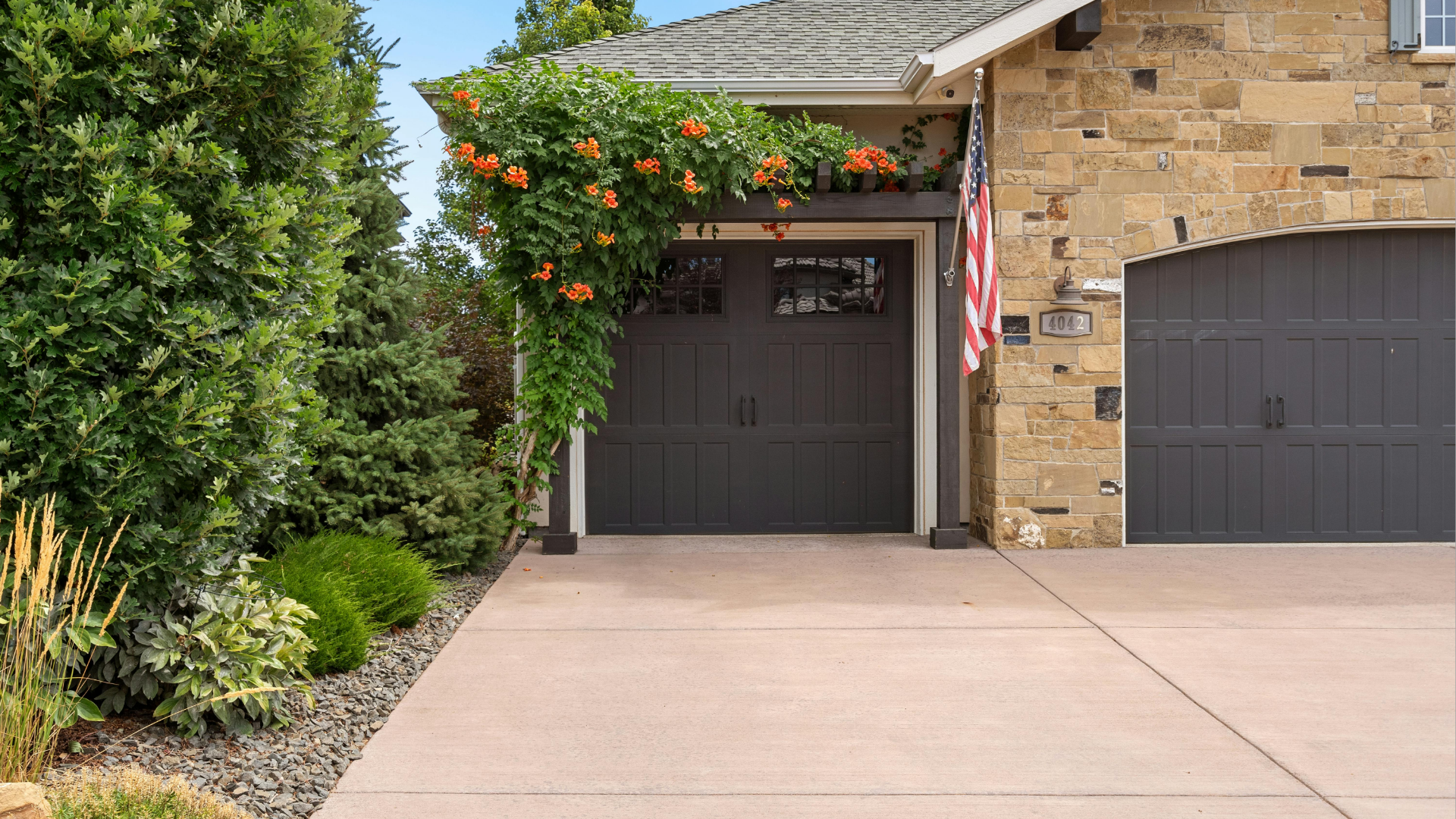 House with dark garage doors, stone facade, orange trumpet vine, and a concrete driveway