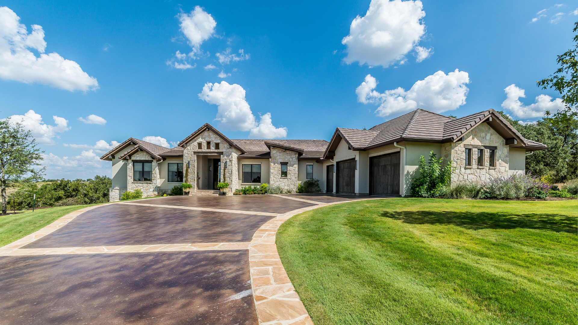 Large stone and stucco house with a paver driveway under a partly cloudy sky