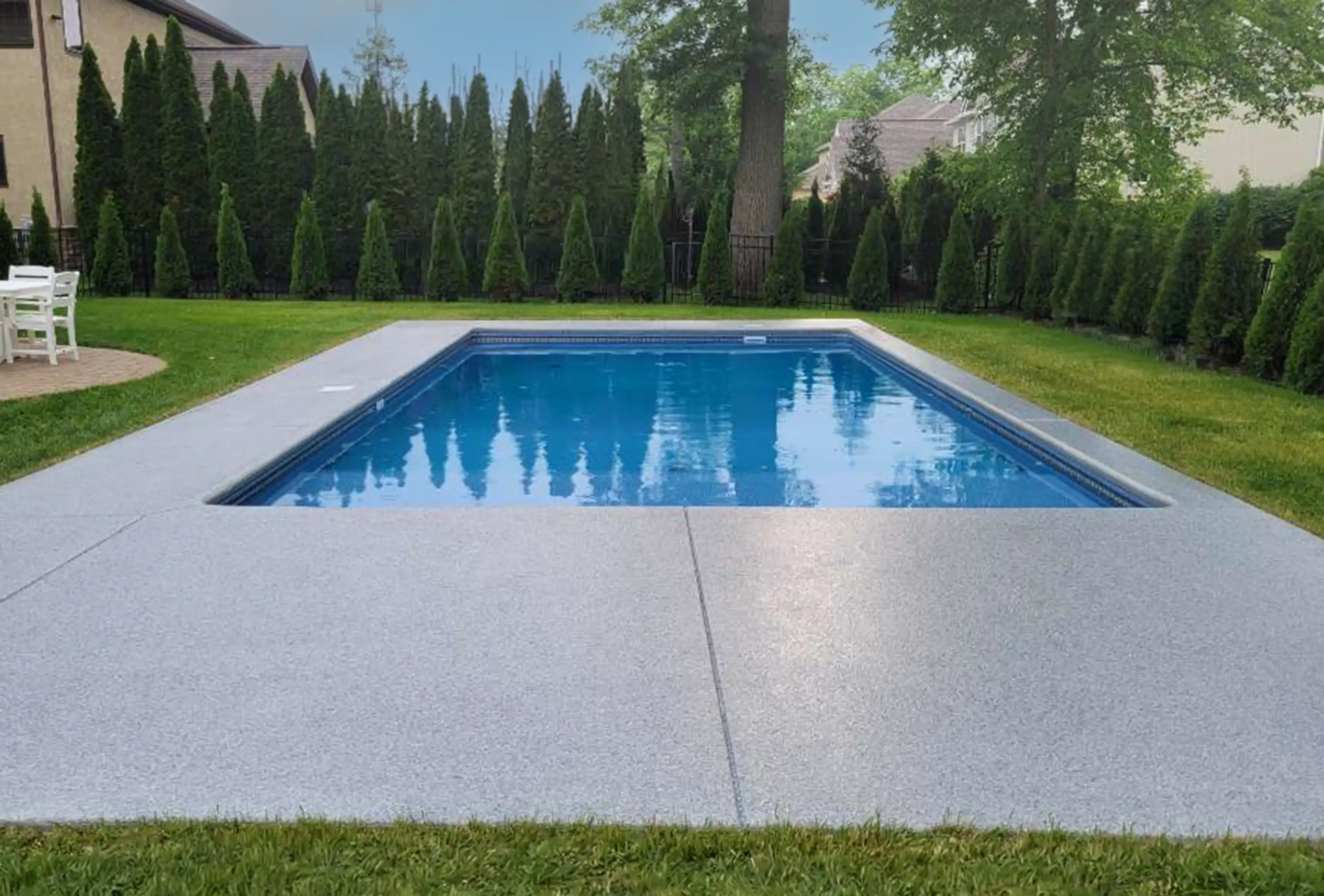 In ground pool with a speckled gray pool deck coating surrounded by manicured evergreen landscaping