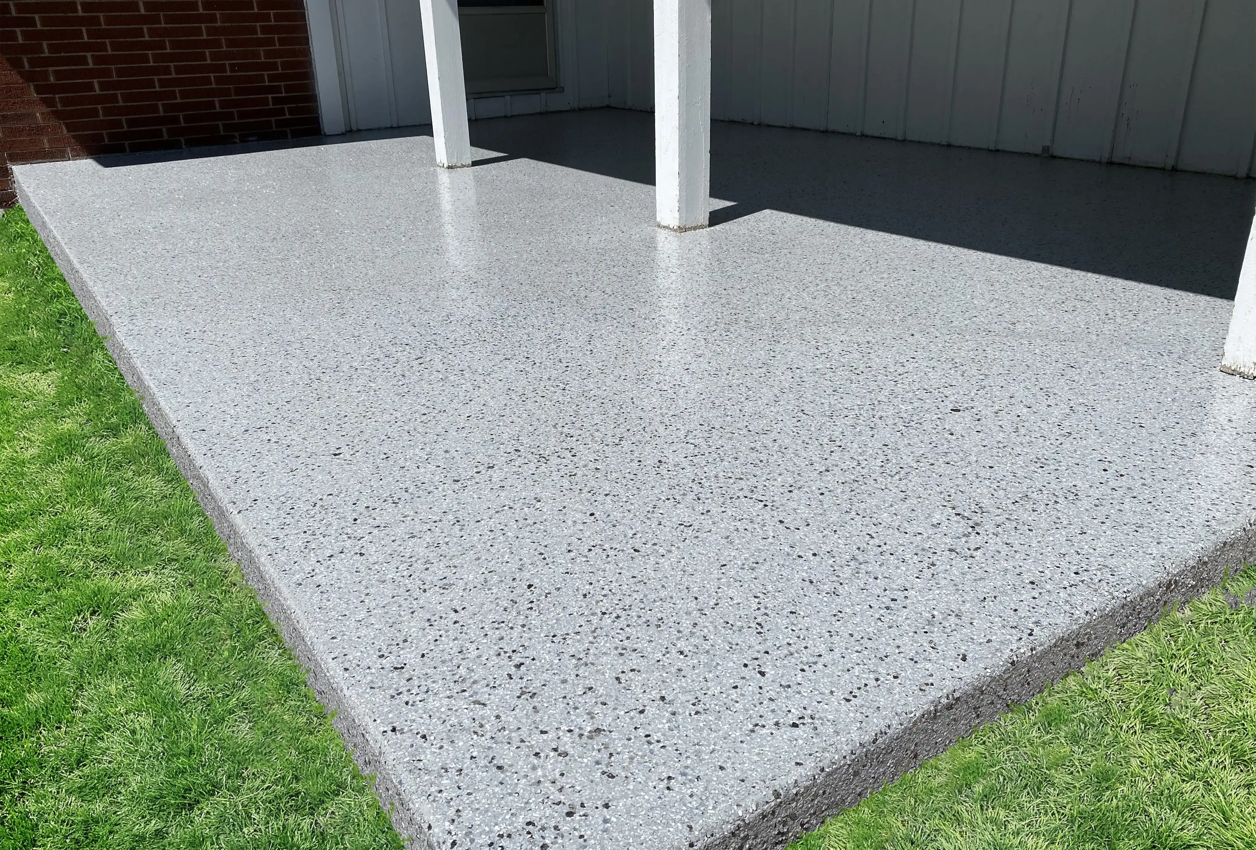 Covered porch with a full flake gray epoxy floor beside a brick wall and white posts