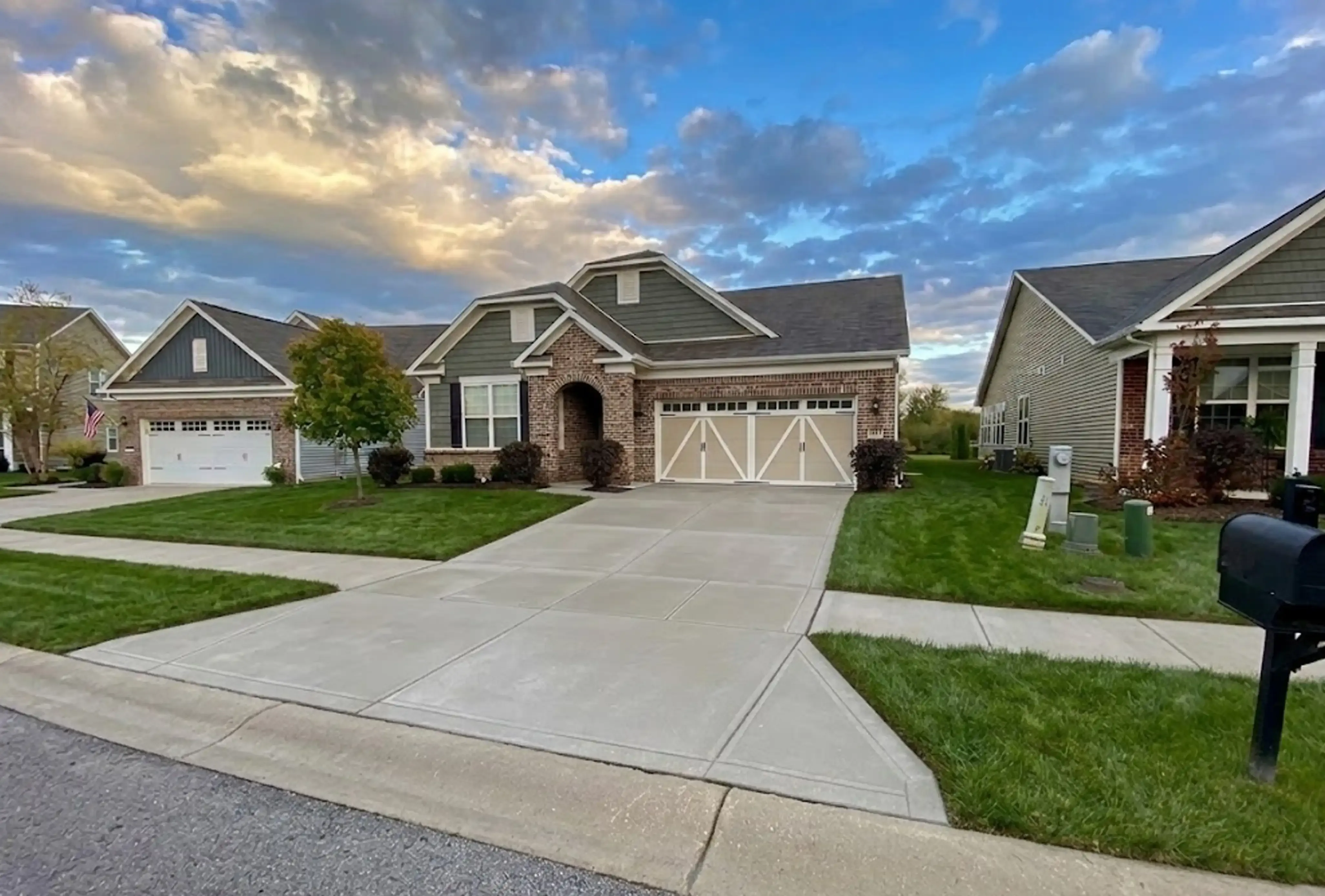 Brick ranch house with two white garage doors and a concrete driveway under a sunset sky