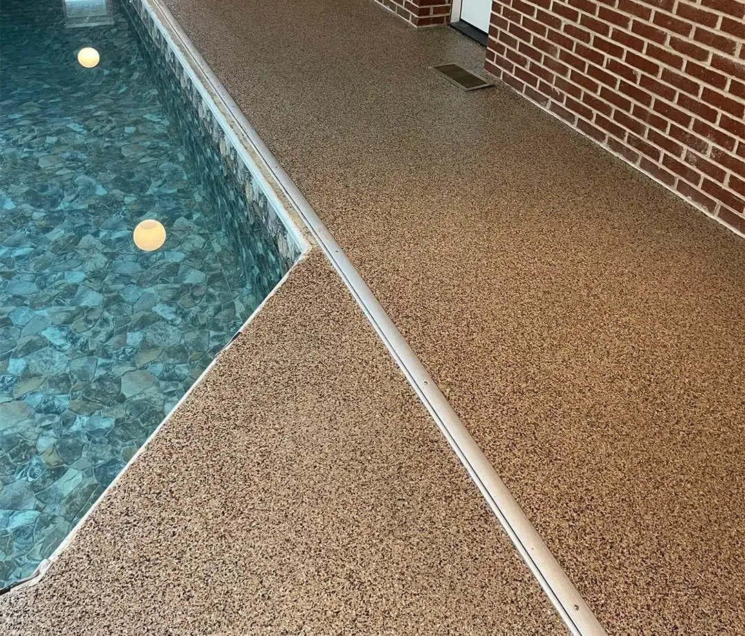 Poolside with a textured tan pool deck coating next to blue water and a brick wall