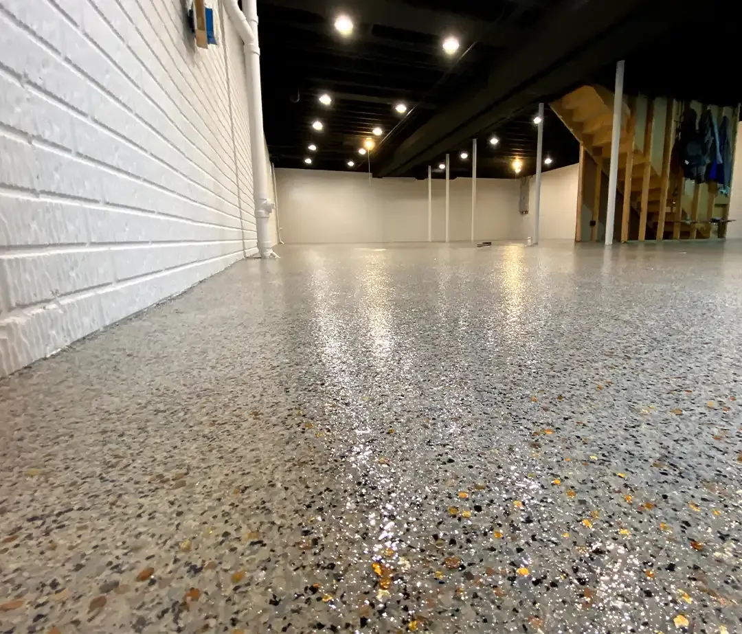 Finished full flake epoxy basement floor with black ceiling beams, white brick-pattern walls and an open staircase