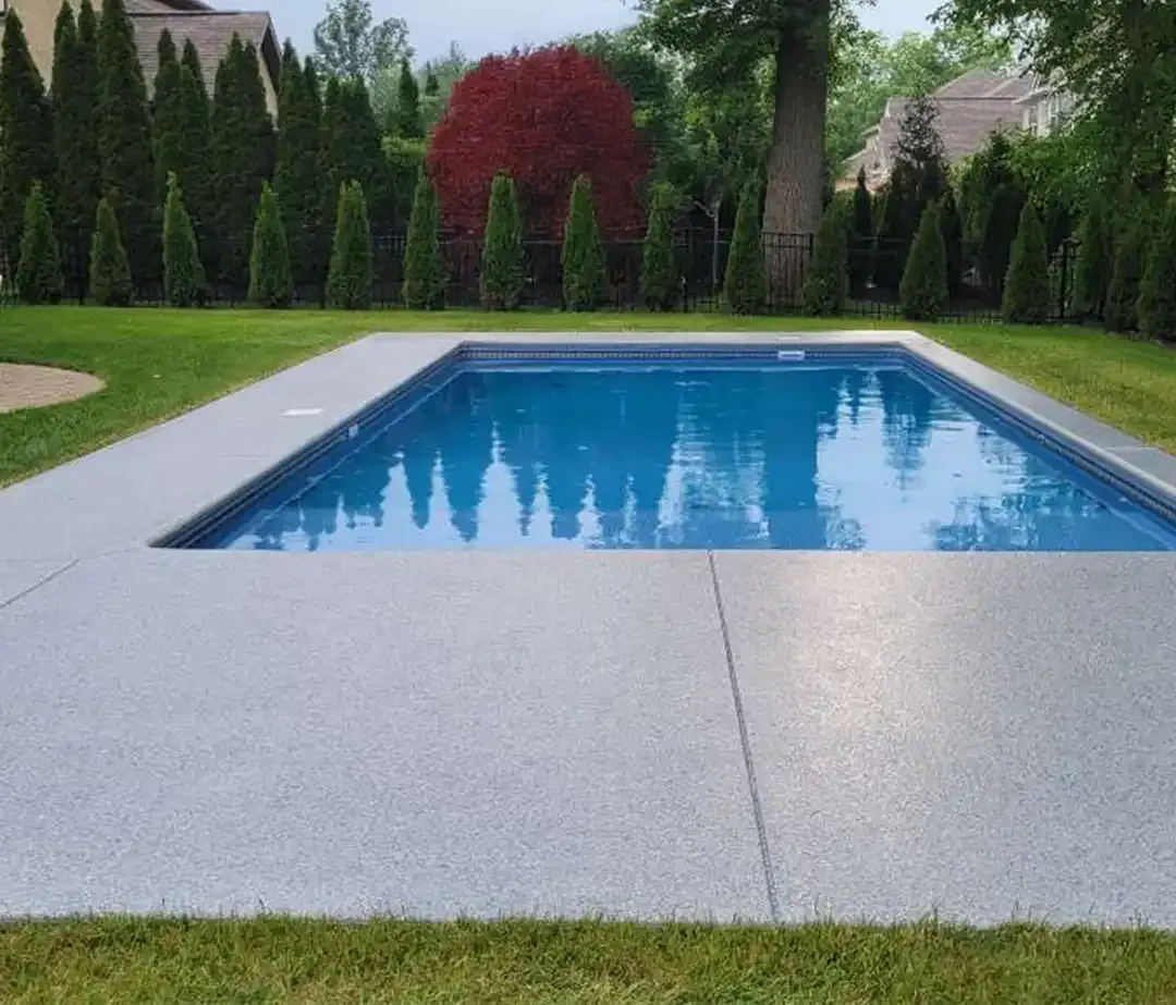 Rectangular pool with a gray pool deck coating surround, grass and trees behind it