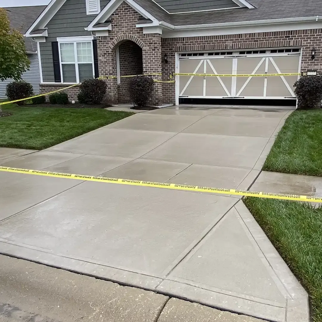 Freshly poured concrete driveway blocked off with yellow GatorGuard caution tape in front of a house
