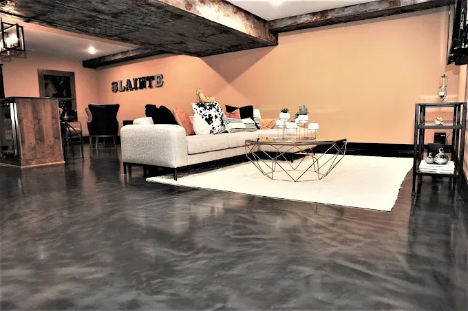 Basement living room with dark metallic epoxy floor, cream sofa, and orange accent wall