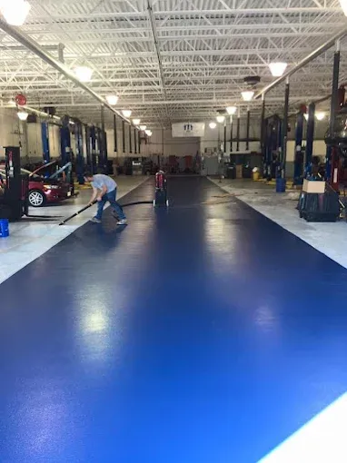 Worker mopping a glossy blue epoxy floor coating in an auto repair shop with cars on lifts
