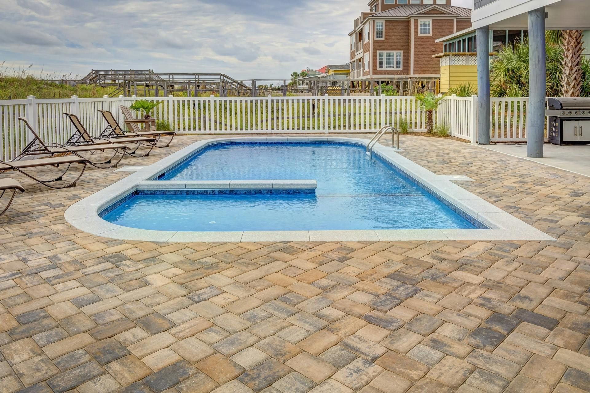 Outdoor pool with a paver deck, lounge chairs and a multi-story beach house