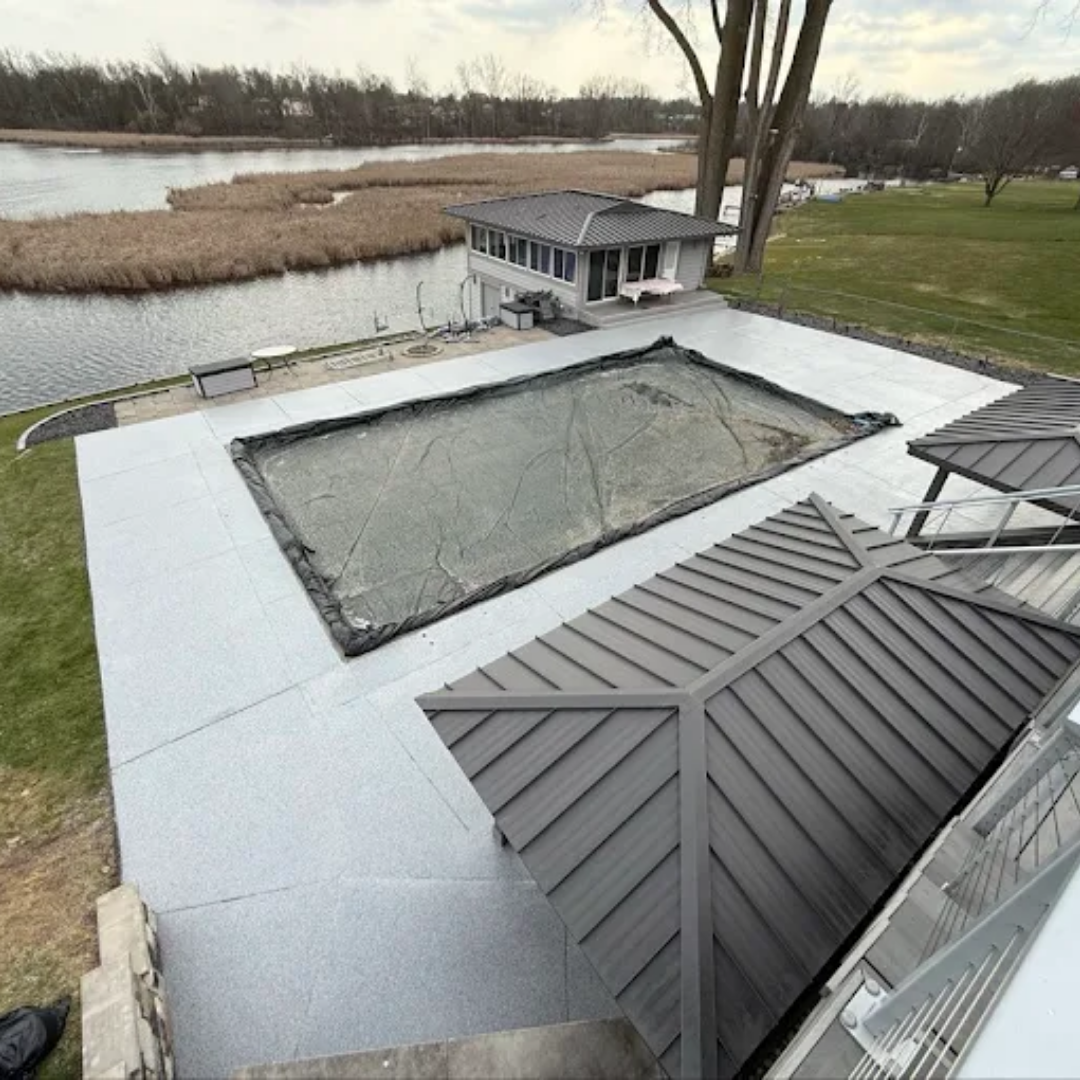 Aerial view of a covered pool with speckled pool deck coating and a lakefront house